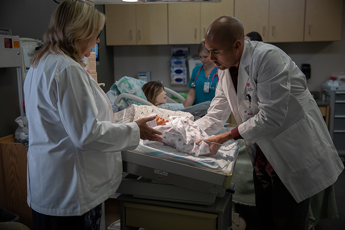 Two doctors holding a attending to a baby and its mother shortly after birth. 